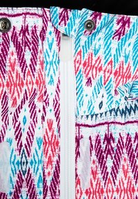 Bunt gemustertes Material mit rosa, lila und blauen geometrischen Designs. Enthält einen zentralen Reißverschluss und Druckknöpfe am Kragen.