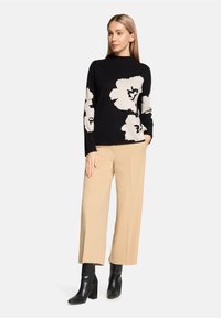 Pull noir en tricot avec de grands motifs floraux blancs, associé à un pantalon large beige et des bottines noires à talons.