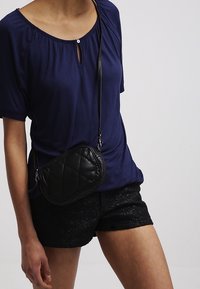 Mörkblå topp med kort ärm och nyckelhålsdetalj, matchad med svarta spetsshorts och en liten kviltad svart axelväska.