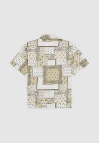 Camisa de manga corta con tela beige que presenta varios patrones geométricos, incluyendo diseños florales y de puntos, dispuestos en parches.