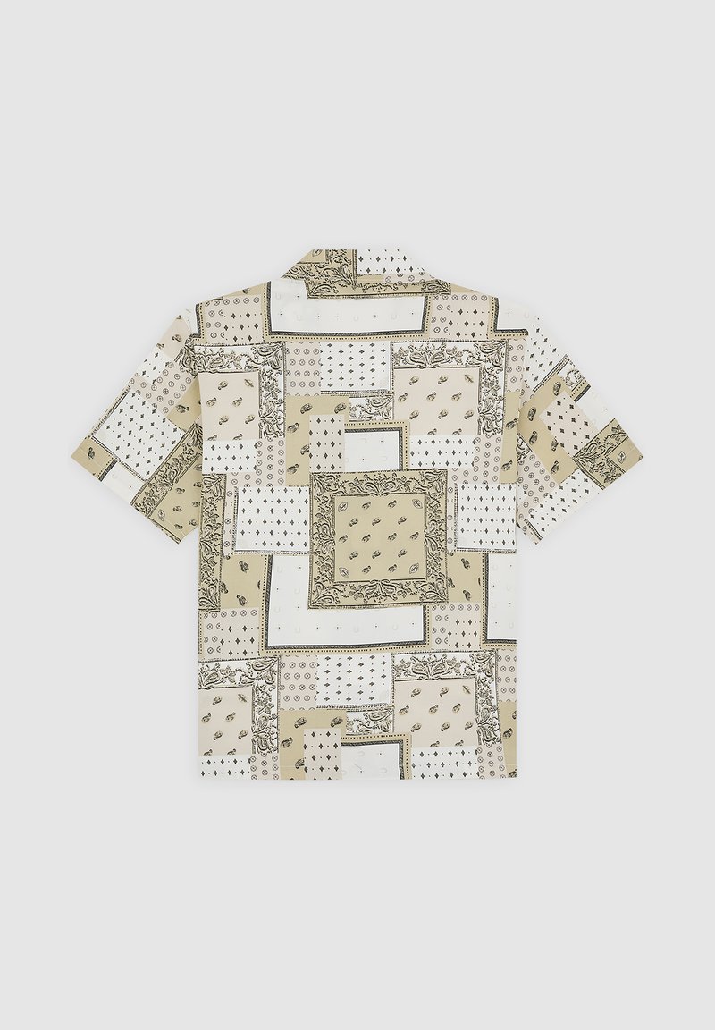 Chemise à manches courtes en tissu beige avec divers motifs géométriques, incluant des dessins floraux et ponctués, disposés en patchs.