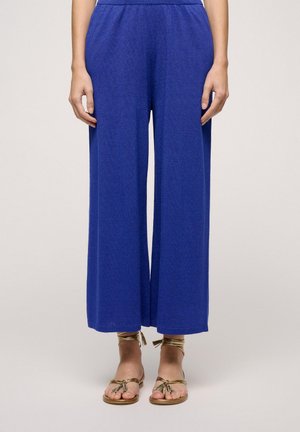Brede broekspijpen in een levendige blauwe kleur, gemaakt van een textuurstof en met een elastische tailleband. Gecombineerd met sandaaltjes met decoratieve veters.