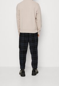 Beżowa bluza z wysokim kołnierzem, zestawiona z czarno-niebieskimi spodniami w kratę. Materiał wydaje się miękki i teksturowany. Uzupełnione czarnymi butami.