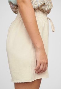 Jupe couleur crème en tissu léger. Présente une taille élastique avec un détail de nouage et une silhouette droite. Texture lisse.