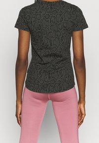 Czarny t-shirt z krótkim rękawem z teksturowanym wzorem wężowej skóry, o dopasowanym kroju i zaokrąglonym dole, zestawiony z różowymi legginsami.