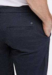 Pantaloni struttura blu navy con una tasca posteriore, caratterizzati da un discreto logo e dettagli di cucitura. Il tessuto appare robusto e resistente.