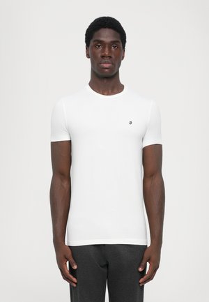 White short-sleeve t-shirt made of soft fabric, featuring a round neckline and a small black logo on the chest, worn with dark pants.