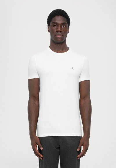 Weißes, kurzärmeliges T-Shirt aus weichem Stoff, mit rundem Halsausschnitt und kleinem schwarzem Logo auf der Brust, getragen mit dunklen Hosen.