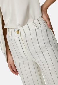 Vita linnbyxor med tunna svarta vertikala ränder, framknappslås och sidofickor. Texturerad duk ger visuell intress. 