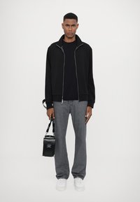 Giacca nera con zip, maglietta nera, jeans grigi e sneakers bianche. Tieni una piccola borsa nera con tracolla. Design semplice e pulito.