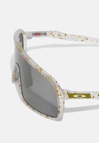 Gafas de sol con montura transparente que presenta un patrón moteado en colores como rosa y dorado, lentes grises y un acento dorado en la patilla.