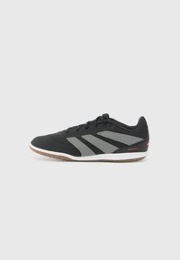 Black athletic shoe with grey accents, perforated texture, rubber sole, and cushioned collar. Features three diagonal stripes and red logo.