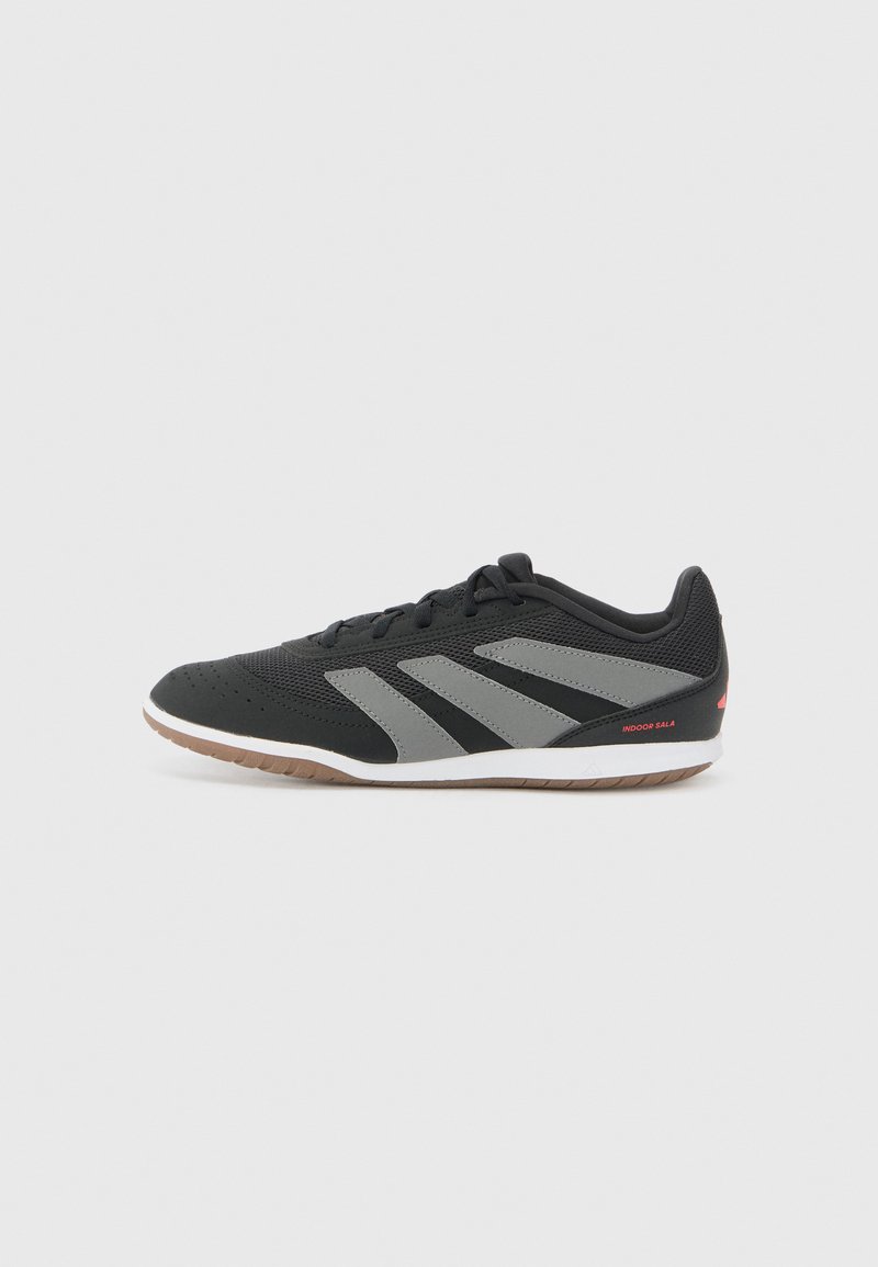 Black athletic shoe with grey accents, perforated texture, rubber sole, and cushioned collar. Features three diagonal stripes and red logo.