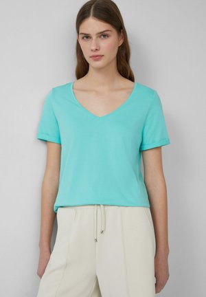T-shirt turquoise à manches courtes en tissu doux, avec des manches retroussées et une coupe décontractée, associé à un jogging beige clair.