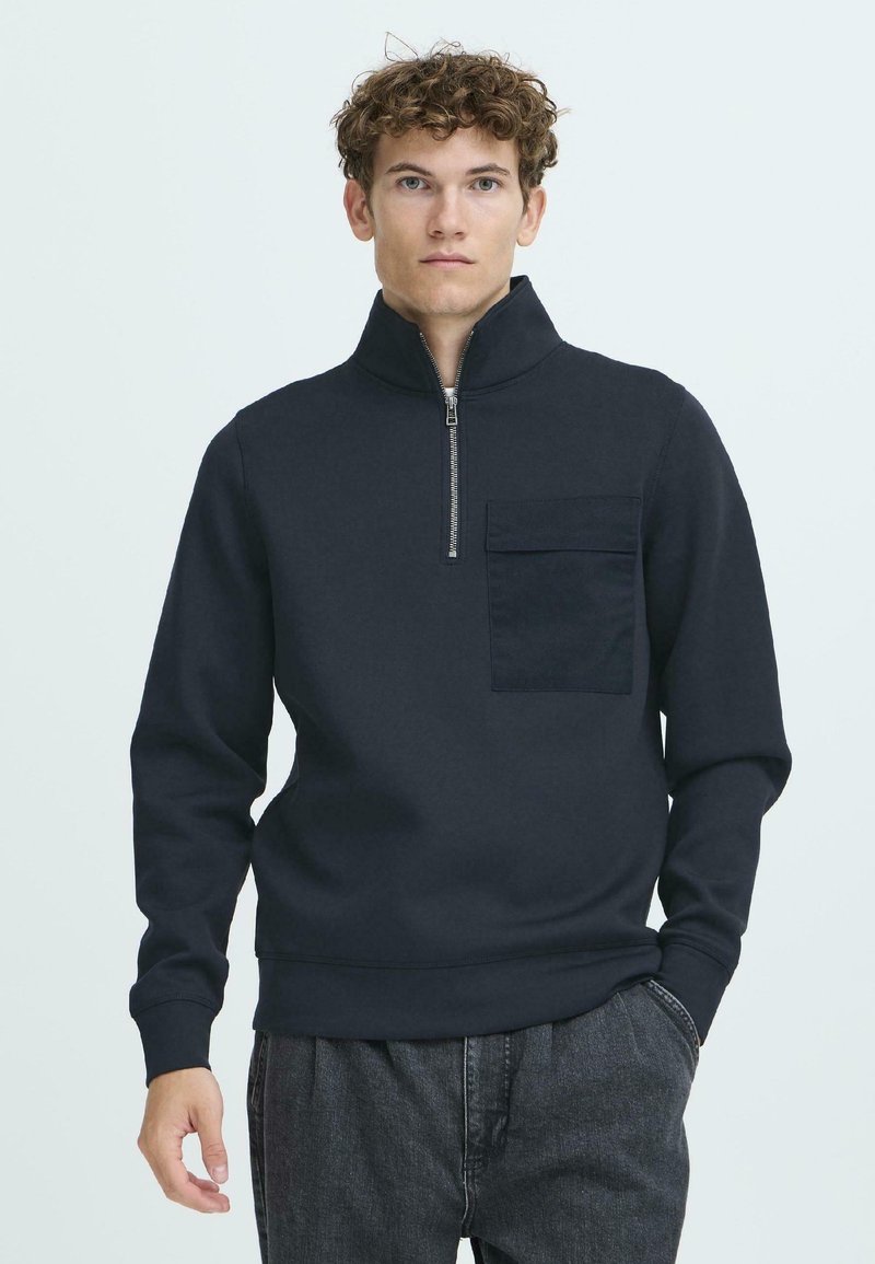 Sweat-shirt zippé bleu marine foncé avec un col haut, une poche avant et des poignets côtelés. Texture lisse et coupe décontractée.