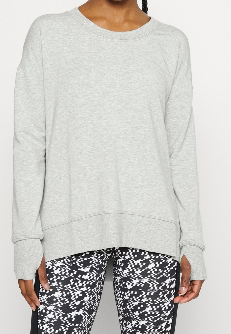 Femme portant un sweat-shirt gris clair à manches longues avec des trous pour les pouces et des leggings à motif pixellisé noir et blanc.