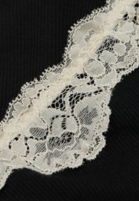 Svart tyg med en strukturerad ribbstruktur har en bred spetskant i off-white, som visar blommönster och delikata kanter.