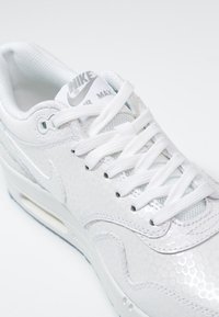 Vita Nike Air Max sneakers med hexagonalt mönster, vita snörning och vadderad krage. Den strömlinjeformade designen inkluderar en logotyp på tungan.