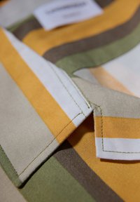 La tela de rayas multicolores presenta líneas amarillas, verdes, marrones y blancas. Las costuras son visibles a lo largo de los bordes, lo que realza la textura.