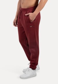 Marlot sweats med elastisk talje, sidelommer og sorte accenter, parret med hvide sneakers. Glat tekstur, afslappet pasform.