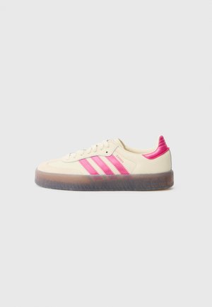 Lavtop cremefarvet sneaker med klare pink striber, hælflap, snørebånd og gummisål, mærket "SAMBA" på siden.