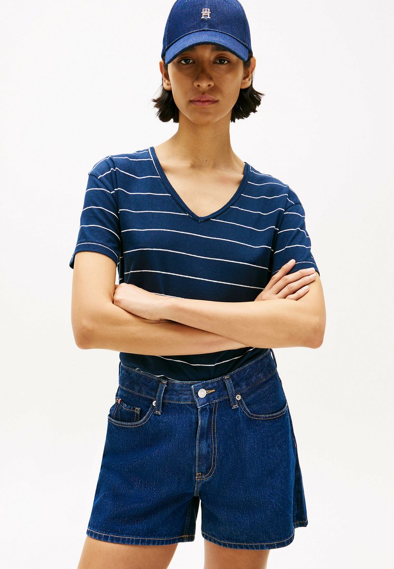 Camiseta de cuello en V a rayas en color marino con mangas cortas, combinada con pantalones cortos de mezclilla azul de tiro alto que cuentan con bolsillos frontales y cierre de botón.