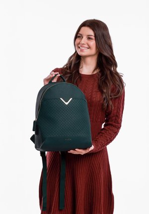Green quilted backpack with a gold accent logo, rounded top, adjustable straps, and a textured finish. Front zipper closure.