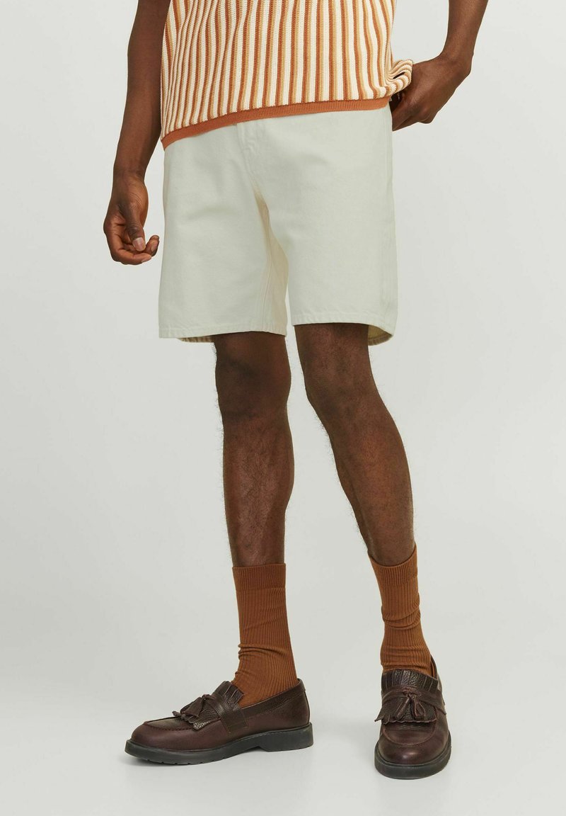 Pantalones cortos de algodón beige con un corte recto, combinados con calcetas marrones acanaladas y zapatos de cuero marrón con un detalle de lazo.