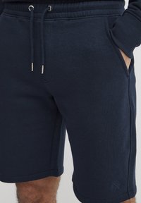 Marineblå bomullsshorts med elastisk linning, snøring og sidelommer. Har et lite logo på den nedre kanten.