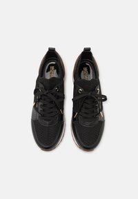 Black athletic shoes featuring a mix of smooth and perforated leather. Knit collar with gold accents. Rounded toe and flexible sole.