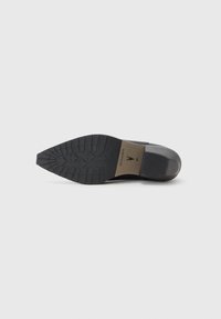 Suela de zapato negra con puntera afilada, goma texturizada para tracción y un acabado suave en el tacón. Presenta la marca "ALLSAINTS".