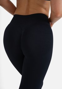 Hochtaillierte schwarze Leggings aus einem glatten, elastischen Stoff. Sie verfügen über einen gerippten Bund und ein enganliegendes Design, das den Körper umschmeichelt.