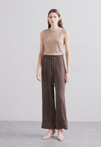 Beige ermeløs topp kombinert med brune vide bukser med mønster som har et geometrisk design, komplettert med nude-fargede hæler.