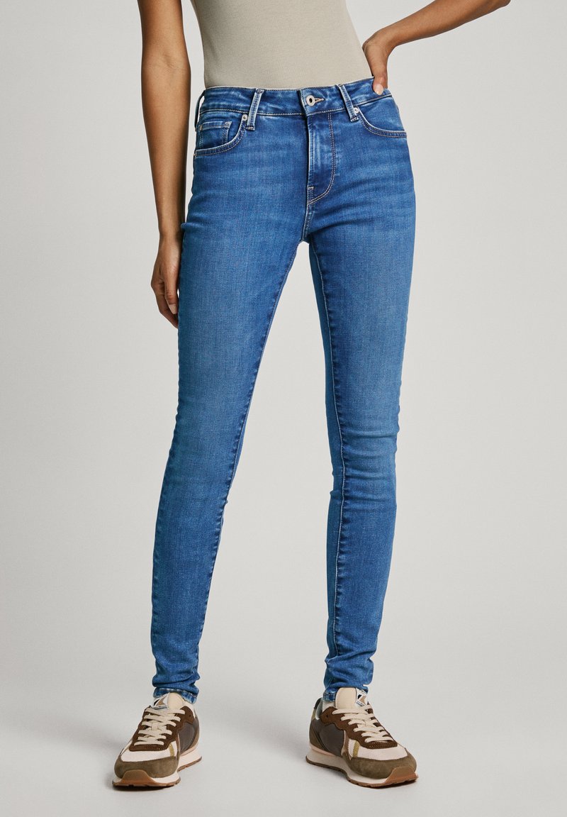 Jeans ajustados azules de denim, con una cintura alta, diseño de cinco bolsillos y costura en contraste. Combinados con zapatillas de deporte multicolores.