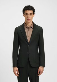 Blazer nero su misura con due bottoni, revers a punta e tasche frontali, indossato sopra una maglietta color marrone chiaro, tessuto morbido e vestibilità strutturata.