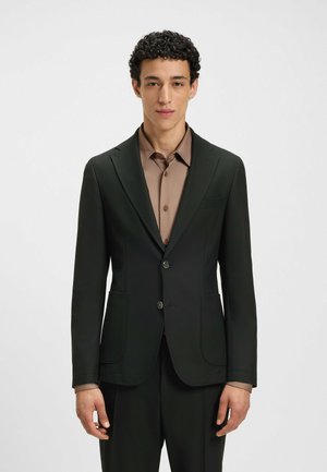 Schwarzer taillierter Blazer mit zwei Knöpfen, Reverskragen und Fronttaschen, getragen über einem hellbraunen Hemd, glattes Material und strukturierte Passform.