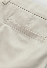 Gros plan sur un tissu beige avec une poche passepoilée horizontale et des détails de couture visibles.