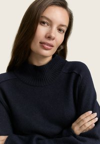 Maglione lavorato a maglia di colore blu navy con colletto alto a coste, tessuto testurizzato e spalle scese, dotato di maniche lunghe e vestibilità rilassata.