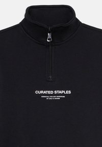 Czarny sweter z zamkiem błyskawicznym do jednej czwartej długości i wysokim kołnierzem, z białym napisem "CURATED STAPLES ESSENTIAL FOR ANY WARDROBE BY ONLY & SONS"