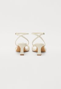 Sandales blanches à talons carrés, dotées de lanières croisées à l'arrière et d'une texture en cuir lisse. Boucle simple.