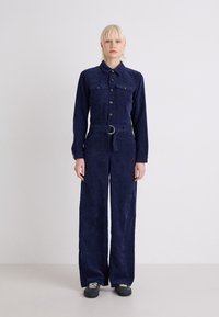 Navy blauwe corduroy jumpsuit met lange mouwen, knoopzakken, een ceintuur in de taille en een wijde pijp, met een gestructureerd oppervlak.