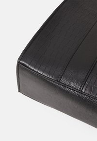 Gros plan d’un coin d’un sac en cuir noir avec des panneaux lisses et à texture crocodile cousus ensemble.