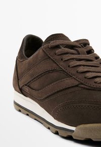 Baskets en daim marron avec une finition texturée, bout rond et semelle intermédiaire blanche contrastante. Comprend des accents de couture et des lacets plats.