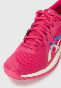 Scarpa sportiva rosa con una tomaia in rete testurizzata, lacci piatti e un logo bianco e blu a contrasto sul lato. Design con punta arrotondata.