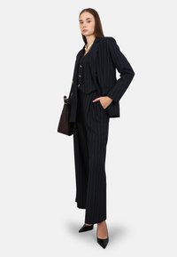 Costume rayé marine avec un blazer court et un pantalon large. Comprend des boutons dorés et une poche. Associé à des talons aiguilles noirs.