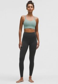 Ljusgrön sportbh med justerbara tunna remmar, i kombination med högmidjade svarta leggings. Båda är tillverkade av ett mjukt, stretchigt tyg.