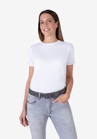 T-shirt bianca in cotone con scollo rotondo, maniche corte, abbinata a jeans grigi chiari e una cintura nera borchiata. Design semplice e casual.