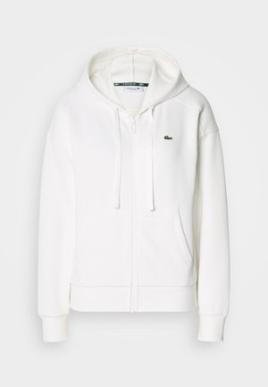 Biely zipsový mikina vyrobená z mäkkej tkaniny, s kapucňou, klokankovými vreckami a malým zeleným logom Lacoste na ľavej hrudi.