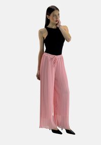 Roze geplooide broeken met een elastische tailleband en bijpassend trekkoord, gecombineerd met een zwarte mouwloze top. Lichte stof, ontspannen pasvorm.