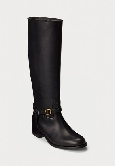 Black knee-high leather boot with a low block heel and decorative strap with gold buckle around the ankle.